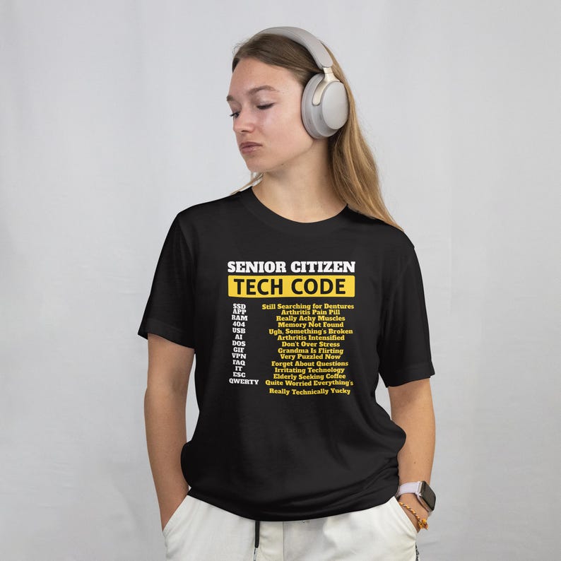 May include: Black t-shirt with the text "SENIOR CITIZEN TECH CODE" in white and yellow. The shirt lists humorous tech-related phrases like "Still Searching for Dentures" and "Memory Not Found".