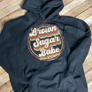May include: Black hooded sweatshirt with a brown, orange, and yellow retro-style graphic that says "Brown Sugar Babe".