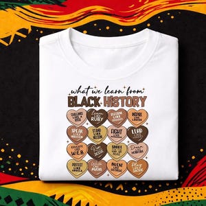Könnte beinhalten: Weißes T-Shirt mit dem Text "what we learn from BLACK HISTORY" und herzförmigen Grafiken mit inspirierenden Phrasen. Das Shirt hat einen Rundhalsausschnitt und ist gefaltet. Der Hintergrund hat ein farbenfrohes Design.