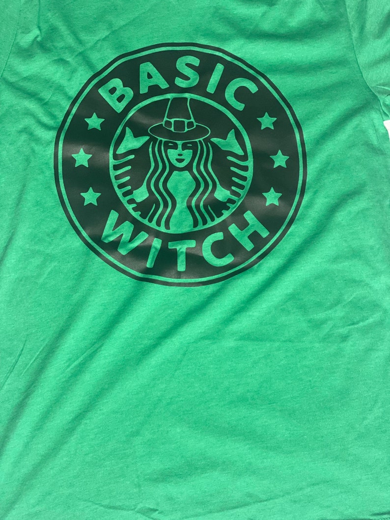 May include: Green t-shirt with a black and white graphic of a witch wearing a hat and the text "BASIC WITCH" in a circle.