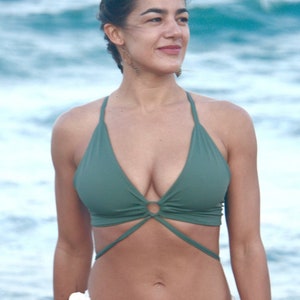 May include: A woman wearing a green halter top bikini with a criss-cross design in the front. She is standing in front of a blue ocean.