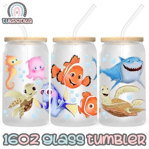 Puede incluir: Tres vasos de vidrio de 473 ml con tapas de bambú y pajitas transparentes. Cada vaso presenta un personaje de dibujos animados diferente de la película "Buscando a Nemo", incluyendo a Nemo, Dory y Bruce el tiburón. El texto "16OZ GLASS TUMBLER" está impreso en la parte inferior.
