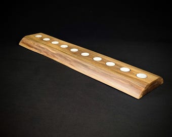 Pode incluir: Um porta-velas de madeira rústico longo com dez poços para velas espaçados uniformemente. O porta-velas é feito de madeira natural de cor castanho claro e ligeiramente curvado.