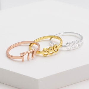 May include: Three gold rings with different names inscribed on them. The rings are stacked on top of each other. The ring on the bottom is rose gold, the middle ring is gold, and the top ring is silver.