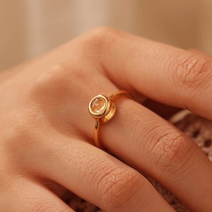 Puede incluir: Un anillo de oro con una piedra preciosa redonda y transparente engastada en un engaste de bisel.