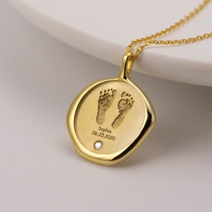 May include: Gold necklace with a round pendant featuring a baby's footprint and the inscription "Sophia 06.20.2020".