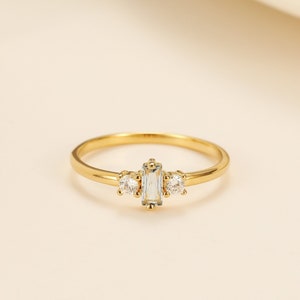 May include: A gold ring with three clear stones. The center stone is a rectangular baguette cut, and the two side stones are round.