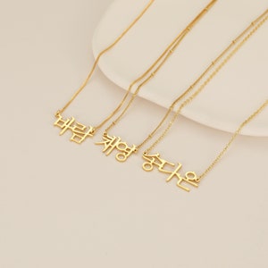 May include: Three gold necklaces with Korean words hanging from them. The words are "바람", "채영", and "승다은".