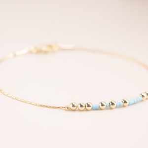 May include: A delicate gold chain bracelet with a row of small gold beads and light blue beads.