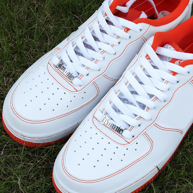 May include: White leather sneakers with red stitching and orange accents. The laces are white and have silver metal aglets that say "JUMPER".
