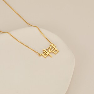 May include: A gold chain necklace with a pendant featuring the Korean word "사랑" in a bold, stylized font.