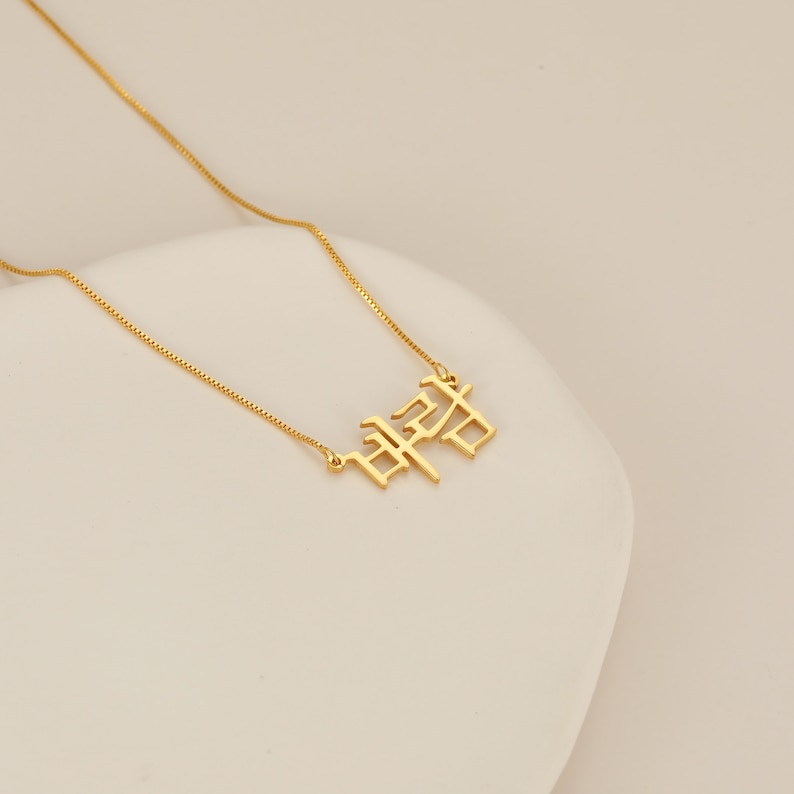 May include: A gold chain necklace with a pendant featuring the Korean word "사랑" in a bold, stylized font.
