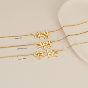 May include: Three gold necklaces with different chain styles: box chain, satellite chain, and cable chain. Each necklace features a pendant with Korean text.