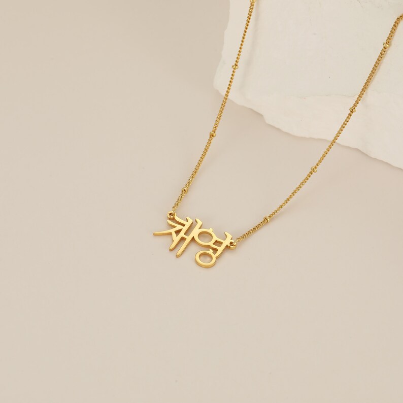 May include: Gold necklace with a delicate chain and a pendant featuring the Korean word "재영" in a simple, modern font.