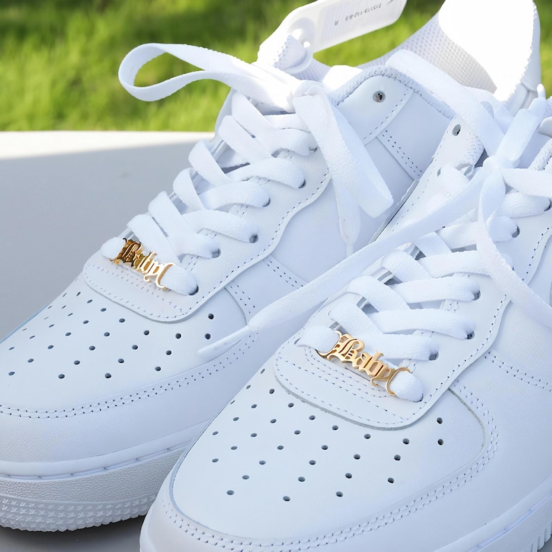 May include: A pair of white leather sneakers with white laces and gold metal lace charms that say "Baby" in a cursive font.