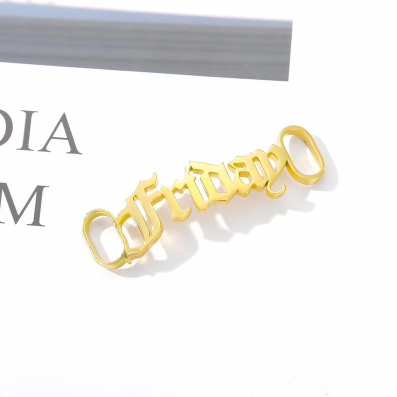 May include: Gold-colored metal charm with the word "Friday" in a gothic font.
