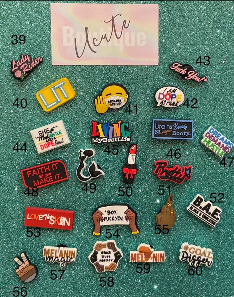 May include: A collection of twenty-two colorful shoe charms featuring various text-based slogans and graphic icons, including a mermaid, lipstick, and hand gestures, each labeled with a number from 39 to 60 on a glittery green background.