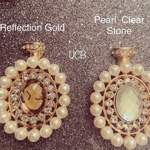 May include: Two gold-toned earrings with a pearl and rhinestone design. The earring on the left has a brown cameo, while the earring on the right has a clear stone.