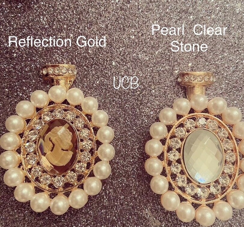 May include: Two gold-toned earrings with a pearl and rhinestone design. The earring on the left has a brown cameo, while the earring on the right has a clear stone.