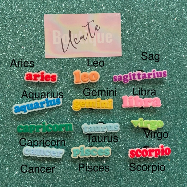 May include: Twelve colorful zodiac sign charms with the names of each sign written in white letters. The charms are arranged in three rows of four. The signs are Aries, Taurus, Gemini, Cancer, Leo, Virgo, Libra, Scorpio, Sagittarius, Capricorn, Aquarius, and Pisces.