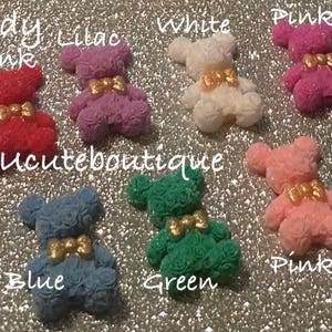 May include: A collection of small bear-shaped figures made of textured rose-like patterns in various colors including hot pink, lilac, white, pink, purple, blue, green, light pink, and black, each featuring a small gold-colored bow at the neck.