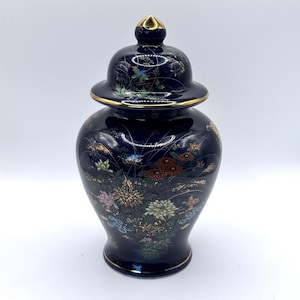 May include: A dark blue ceramic jar with a lid, featuring a floral design in gold, red, and other colors. The jar has a gold rim and a gold finial on the lid. The overall design is ornate and decorative.