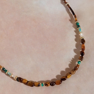 May include: A brown and gold beaded necklace with green and white accents. The necklace is made of tiger's eye, turquoise, and pearl beads.