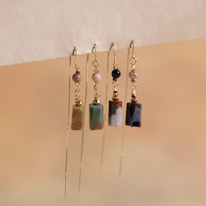 Puede incluir: Cuatro pares de pendientes colgantes de oro con cuentas de piedra de diferentes colores y abalorios rectangulares de piedra. Las piedras son verdes, marrones, blancas y negras.