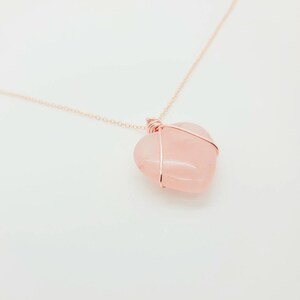 May include: A rose quartz heart pendant necklace. The heart-shaped stone is a soft pink color and is wrapped in a copper-colored wire. The chain is also copper-colored and delicate.