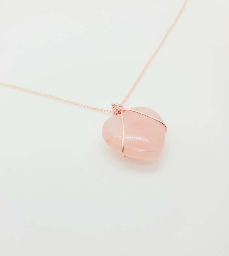 May include: A rose quartz heart pendant necklace. The heart-shaped stone is a soft pink color and is wrapped in a copper-colored wire. The chain is also copper-colored and delicate.