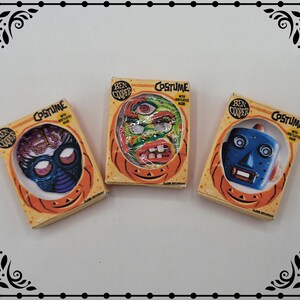 May include: Three vintage Halloween costume boxes with masks. The boxes are yellow with orange and black accents. The masks are a blue robot, a green monster, and a purple alien. The boxes have the text "Ben Cooper Costume with Ventilated Mask" on them.