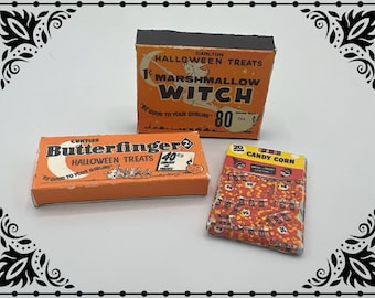 Puede incluir: Tres cajas de golosinas de Halloween vintage. Las cajas son de color naranja y blanco con letras negras. Las cajas están etiquetadas como "Butterfinger Halloween Treats", "Marshmallow Witch" y "Candy Corn".