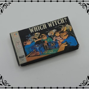 以下が含まれることがあります： 「Which Witch?」というタイトルが黒地に白で印刷された、ビンテージのボードゲームの箱。箱には、魔女とゲームをしている子供たちのカラフルなイラストが描かれています。