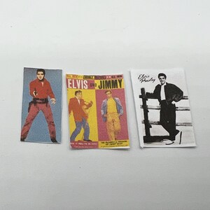 Puede incluir: Tres portadas de &aacute;lbumes de discos vintage con Elvis Presley. La primera portada es un primer plano de Elvis con una camisa roja y pantalones vaqueros azules. La segunda portada presenta a Elvis y Jimmy, con Elvis con una chaqueta roja y Jimmy con una camisa amarilla. La tercera portada es una foto en blanco y negro de Elvis con una chaqueta negra.