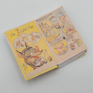 May include: A yellow and white children's book titled "The 3 Little Pigs" with illustrations of a wolf and pigs. The book is open to a page showing the wolf with a toothbrush.