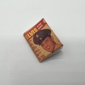 Puede incluir: Una portada de revista vintage con Elvis Presley en su uniforme del ej&eacute;rcito. La portada est&aacute; amarillenta por el paso del tiempo y tiene el t&iacute;tulo "Elvis in the Army" impreso en rojo y negro.