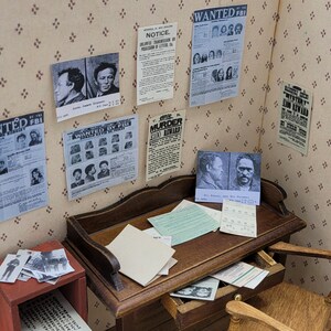 May include: A miniature detective's office with a wooden desk, a chair, and a small red shelf. The walls are covered in wanted posters with black and white photos of people. The posters have the text "WANTED BY THE FBI" and "MURDER - $100 REWARD!"