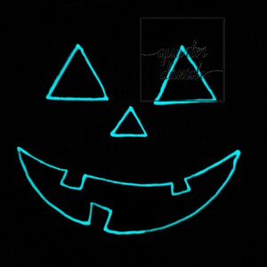 Op de afbeelding: Een zwarte achtergrond met een gloeiend turquoisegroen jack-o'-lantern gezicht. Het gezicht heeft twee driehoekige ogen, een driehoekige neus en een brede, gebogen mond.