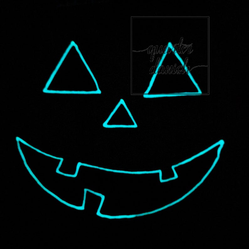 Op de afbeelding: Een zwarte achtergrond met een gloeiend turquoisegroen jack-o'-lantern gezicht. Het gezicht heeft twee driehoekige ogen, een driehoekige neus en een brede, gebogen mond.