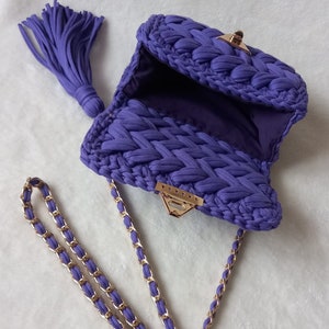 May include: A purple crocheted handbag with a gold chain strap and a tassel. The bag has a clasp closure.