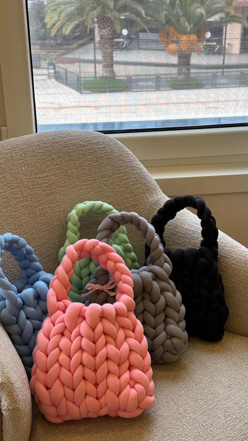 Puede incluir: Cinco bolsas de mano de punto en diferentes colores, incluyendo rosa, azul, gris y verde. Las bolsas est&aacute;n hechas de hilo grueso y tienen un dise&ntilde;o simple y minimalista.