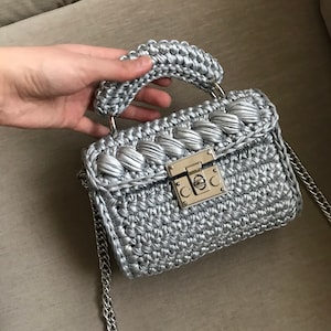 May include: A silver crocheted handbag with a silver chain strap and a gold lock closure.