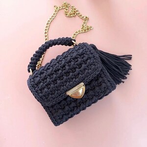 May include: A dark blue crocheted handbag with a gold chain strap and a tassel. The bag has a flap closure with a gold clasp.