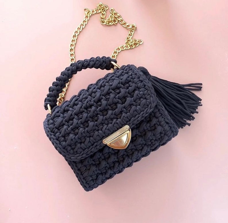 May include: A dark blue crocheted handbag with a gold chain strap and a tassel. The bag has a flap closure with a gold clasp.