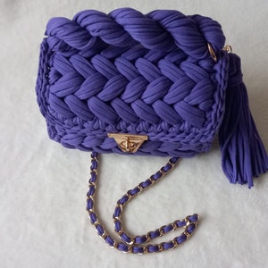 May include: A purple crocheted handbag with a gold chain strap and a tassel.
