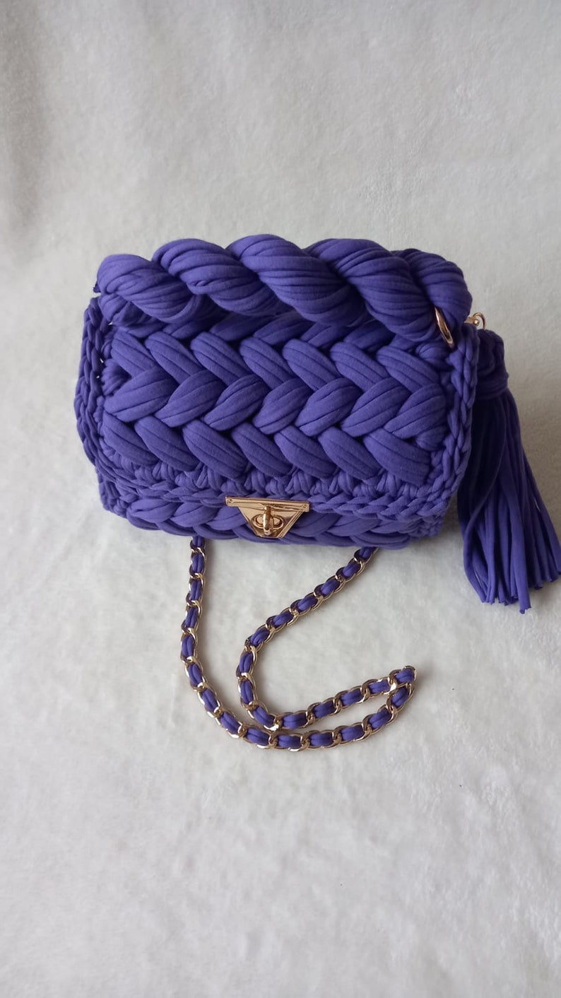 May include: A purple crocheted handbag with a gold chain strap and a tassel.