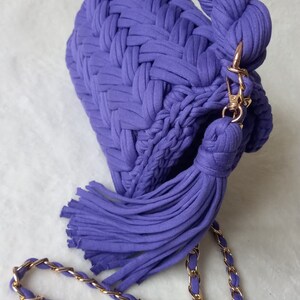 May include: A purple crocheted handbag with a long tassel and a gold chain strap.