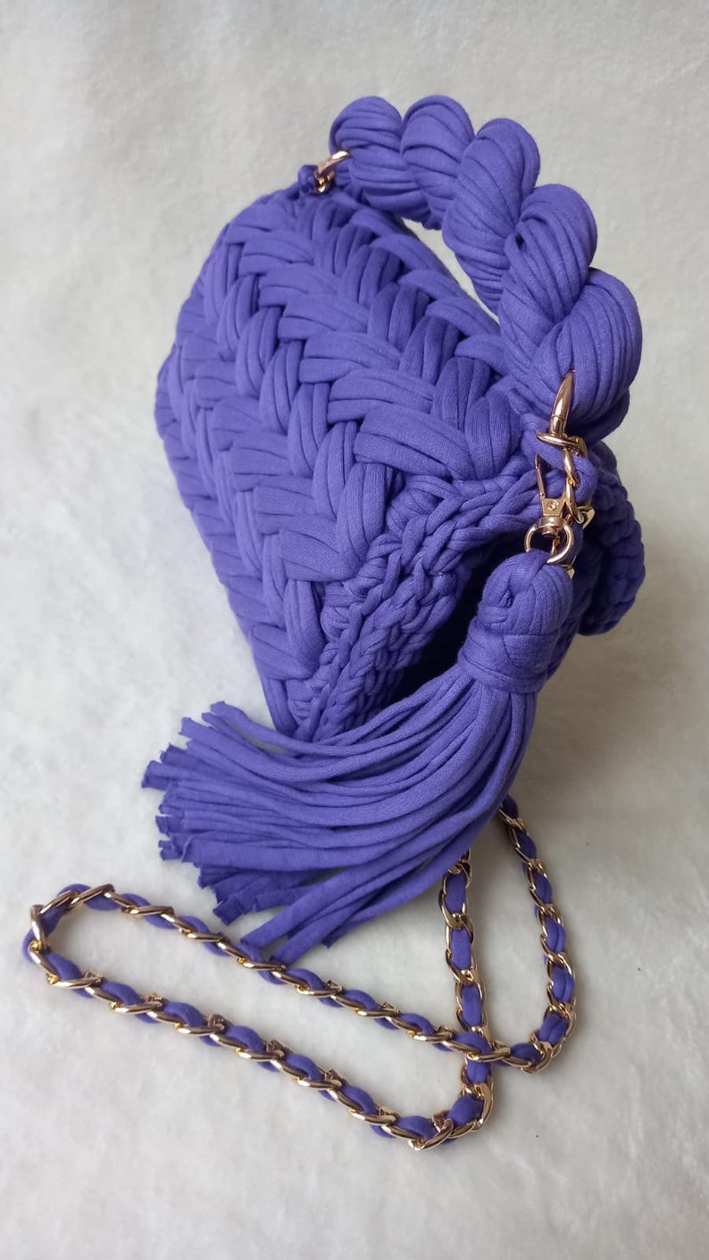 May include: A purple crocheted handbag with a long tassel and a gold chain strap.