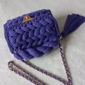 May include: A purple crocheted handbag with a gold chain strap and a tassel.