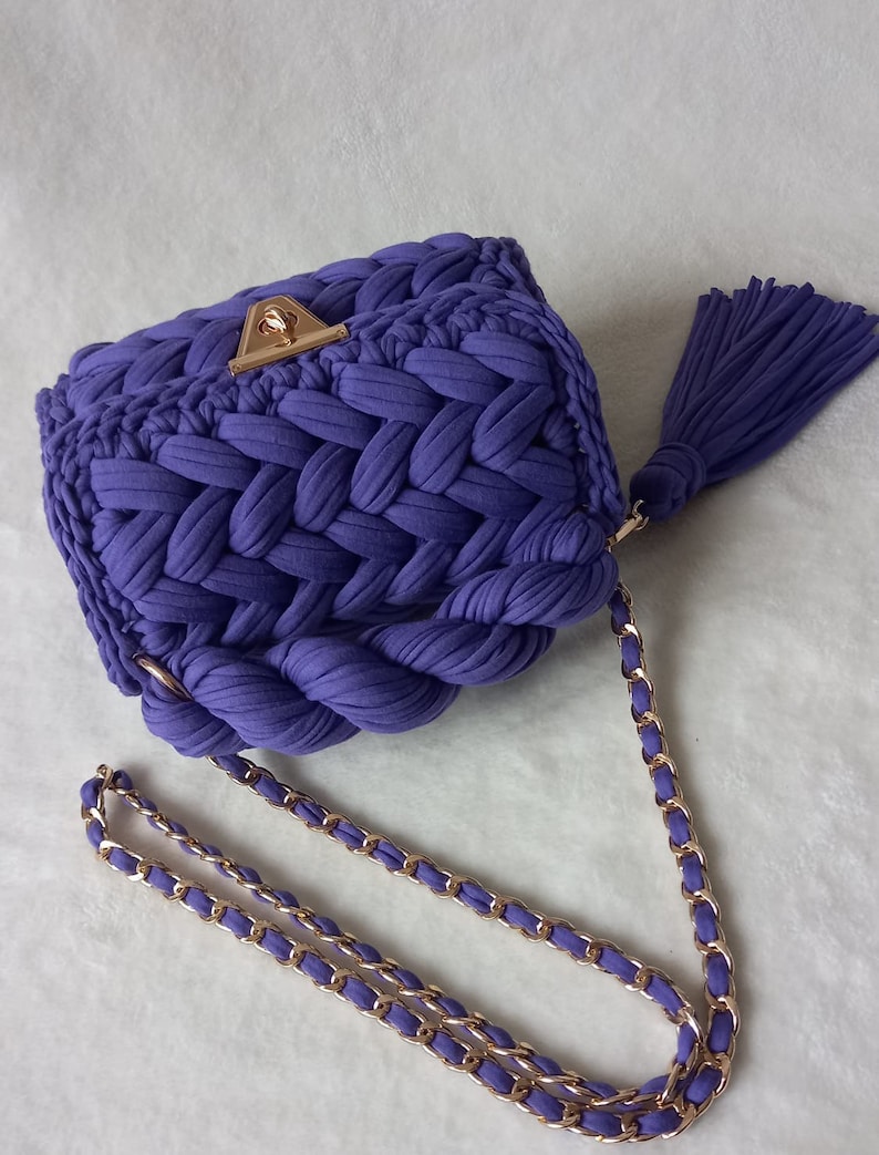 May include: A purple crocheted handbag with a gold chain strap and a tassel.
